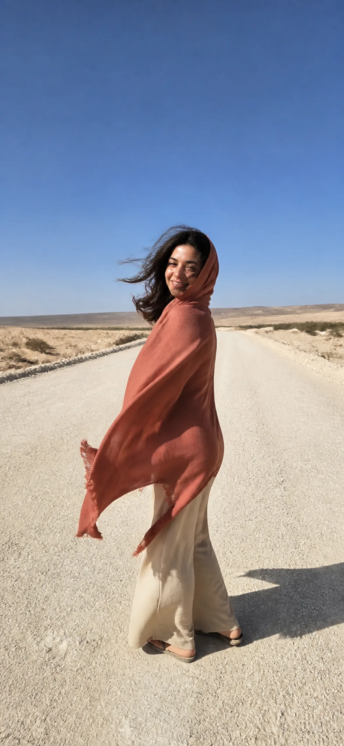 iPhone lock screen wallpaper — woman in a wind-caught scarf on a desert road