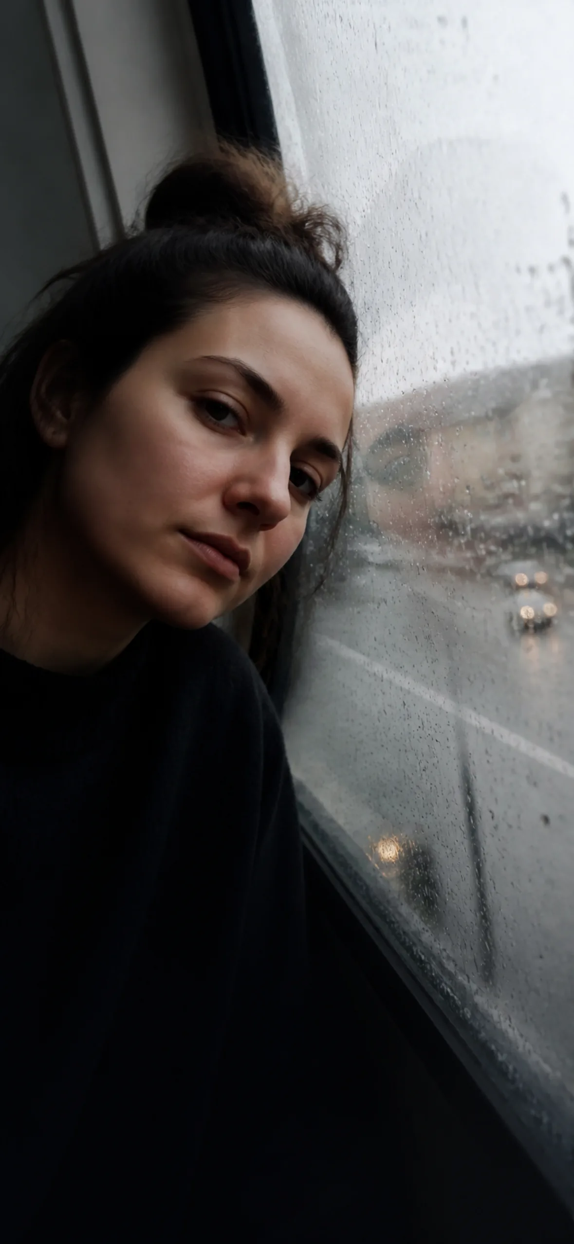 4k phone wallpaper — woman resting against a rain-streaked window