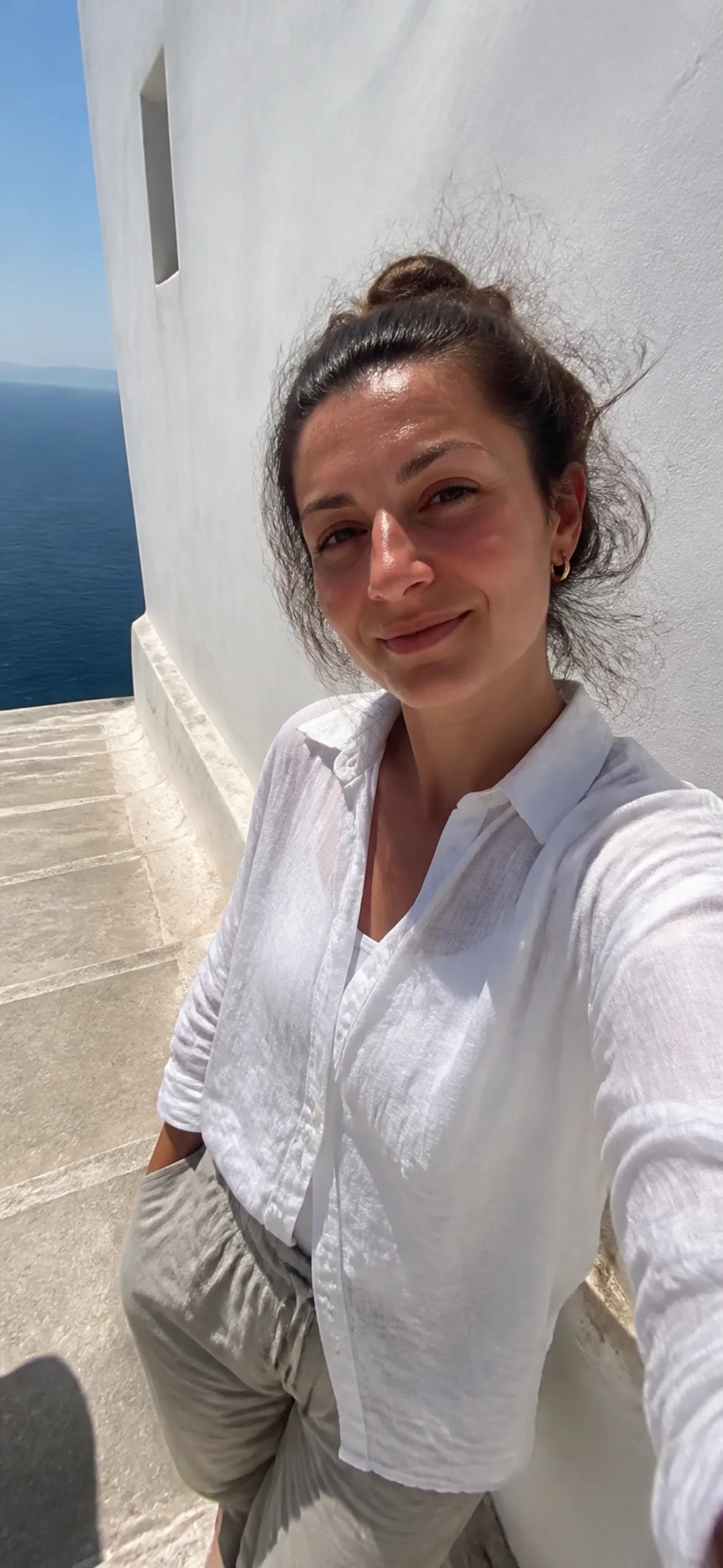 Phone wallpaper — woman in white linen against a sunlit Mediterranean wall